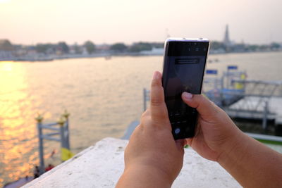 Midsection of person photographing using mobile phone in water