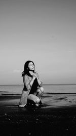 Full length of woman sitting on beach against sky