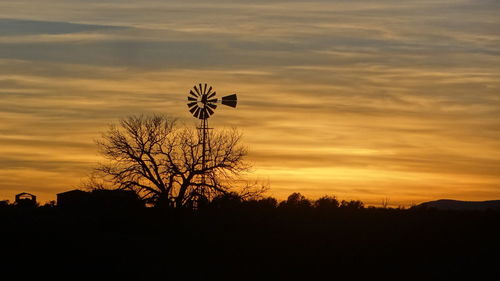 Silhouette trees on landscape against orange sky