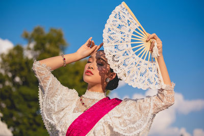 Girl holding hand fan against sky