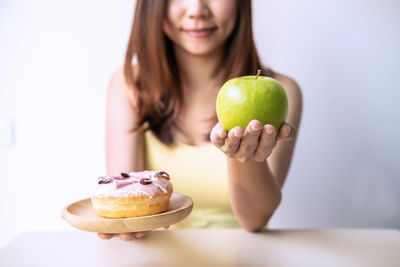 Midsection of woman holding apple and donut while sitting at table