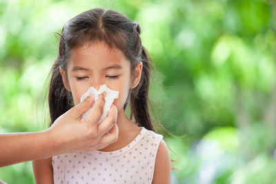 Cropped hand wiping nose of girl with tissue paper