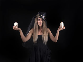 Portrait of young woman standing against black background