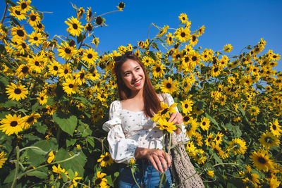 Portrait of smiling young woman against yellow flowering plants