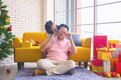 Cute girl covering eyes of father while sitting on sofa at home