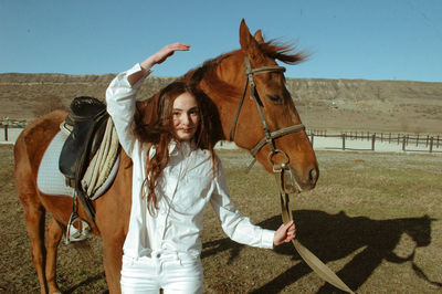 Portrait of young woman with horse standing on land against clear sky