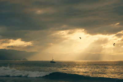 Scenic view of sea against sky during sunset. a boat and a magical golden light from cloudy sky.