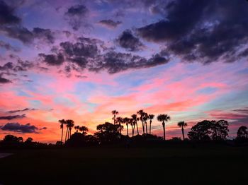 Silhouette trees on landscape against dramatic sky