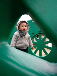 Portrait of cute worried baby boy at playground seen through outdoor play equipment