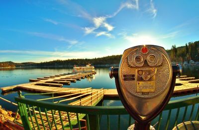 Coin-operated binocular by lake against sky