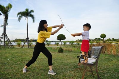 Brother and sister playing with wire on field against sky