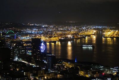 Illuminated city by river against sky at night