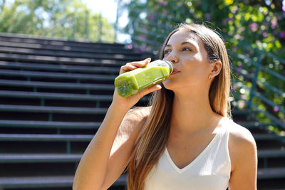 Beautiful healthy young woman drinking green smoothie detox juice outdoors