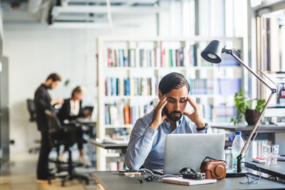 Frustrated businessman looking at laptop while sitting in office