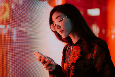 Close-up of young woman using mobile phone standing outdoors at night