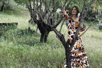 Smiling woman looking away while standing by tree