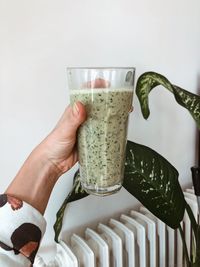 Cropped hand holding smoothie against wall