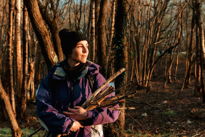 Peaceful young female hiker in warm clothes collecting wood during camping in autumn forest