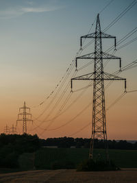 Low angle view of silhouette electricity pylon on field against sky
