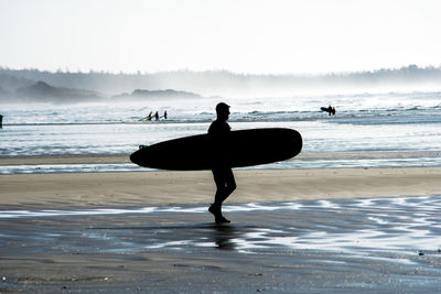 Silhouette of man with surfboard walking at beach