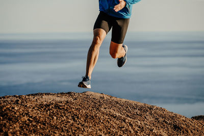 Low section of man running on rock by sea against sky