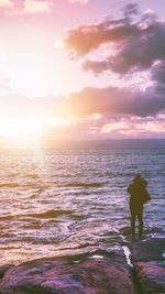 Rear view of silhouette woman standing at beach during sunset