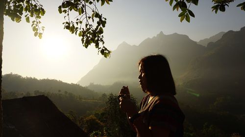 Woman drinking coffee by mountains against sky