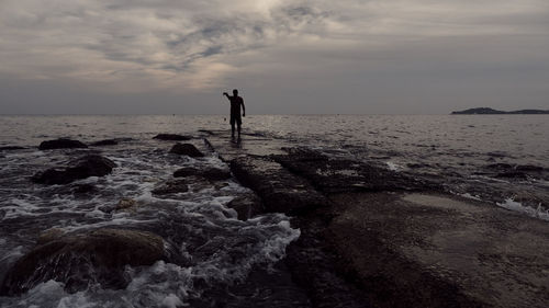 Silhouette man standing on beach against sky during sunset