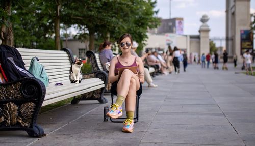 Full length of woman sitting on footpath in city