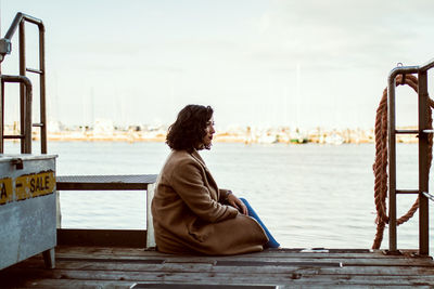 Rear view of woman sitting on retaining wall against sky