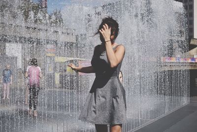 Woman standing by splashing fountain water in city