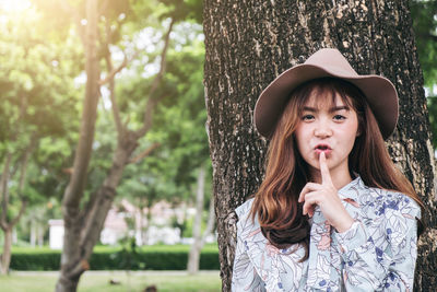 Portrait of young woman with finger on lips at park