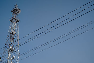 Low angle view of electricity pylon against clear blue sky