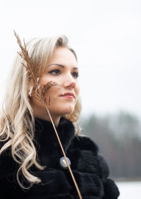 Close-up of young woman looking away while standing against sky at beach