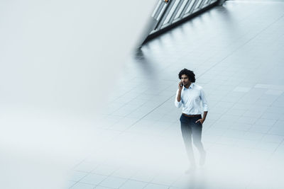 Young male professional talking on mobile phone while walking in office corridor