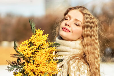 Portrait of a young woman with blond hair holding a bouquet of mimosa in her hands. spring.