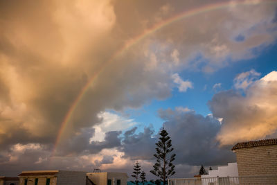 Low angle view of rainbow over houses against sky