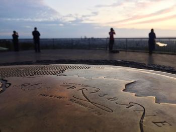 Close-up of map with people standing in background during sunset