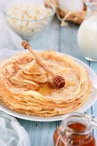 Homemade thin crepe pancakes with honey stacked in a stack, on a table with a pot of milk, a bowl