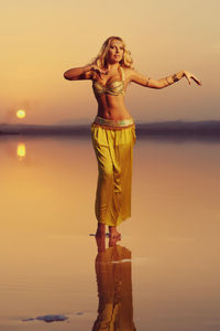 Young woman standing at beach against sky during sunset