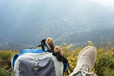 Hiking backpack, trekking poles and legs in sports shoes of young woman resting in mountain hike 