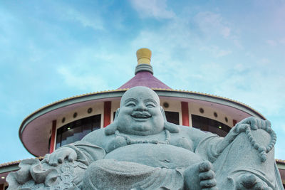 Low angle view of laughing buddha statue against sky