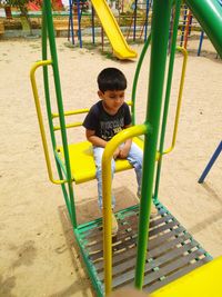 Full length of boy sitting on slide at playground