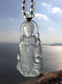 Close-up of buddha pendant by sea against sky