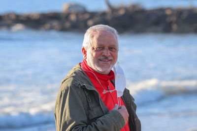 Portrait of smiling senior man standing against sea during winter