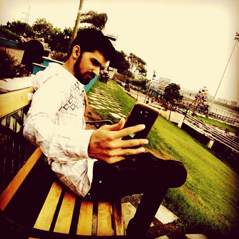 YOUNG MAN USING MOBILE PHONE WHILE SITTING ON WALL