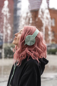 Smiling young woman with pink hair listening music through headphones