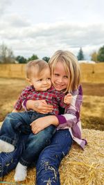 Smiling girl with brother sitting on haystack