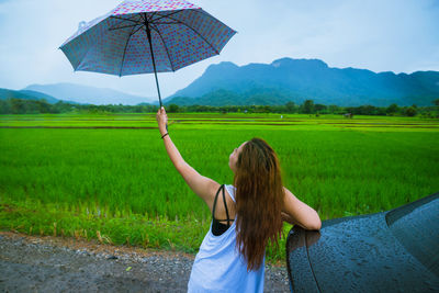 Rear view of woman holding umbrella while standing by car on road