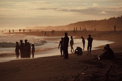 People at beach against sky during sunset